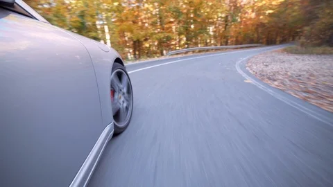 Low angle moving shot of a Porsche 911 Carrera 4s car driving on a forest road Stock Footage 122287320