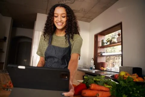 Low angle of Multi-cultural young female reading recipe from tablet while Stock Photos