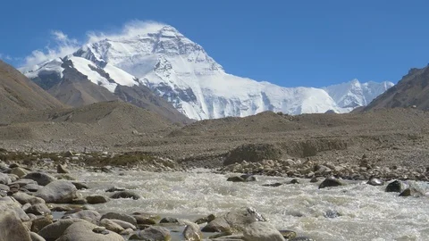 LOW ANGLE: Murky river flows across the rocky foothills of snowy Mount Everest. Stock Footage 112982086