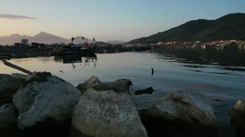 Low angle pan against rocks of fishing village bay at sunset Stock Footage 147984054