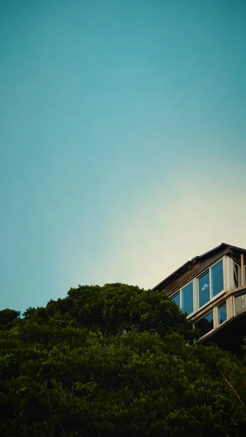 Low angle pan revealing a modern house on a green hill and blue sky Vidéo 345794357