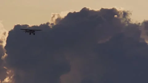 Low angle pan of Super Cub plane flying adjacent nimbus clouds at sunset Stock Footage 252382636