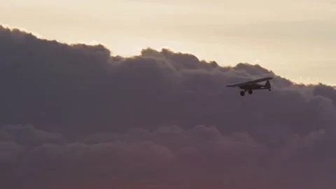 Low angle pan of Super Cub plane flying adjacent nimbus clouds during sunset Stock Footage 252382853