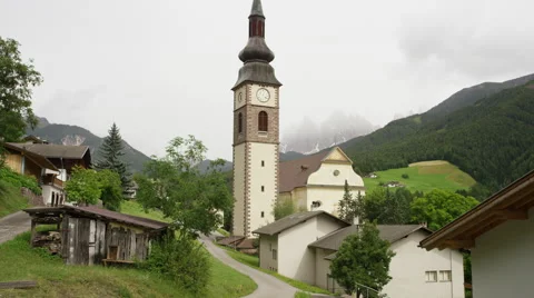 Low angle panning shot of church and clock tower in rural village / Funes, Italy Video stock 43632073