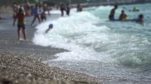 Low angle perspective pebble beach. Sea waves breaking shore. Children playing Stock Footage 335763622