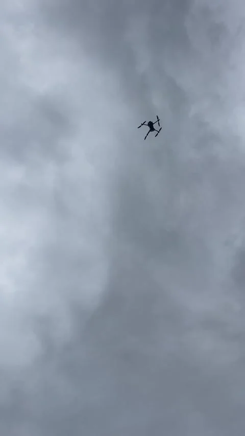 Low-angle pilot operating remote controller while drone flies overhead against Vidéo 344584231