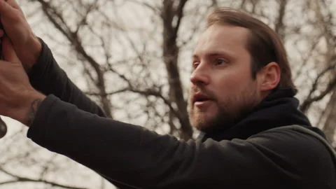 Low angle portrait of bearded man swinging sword with both hands in leafless Stock Footage 347621074