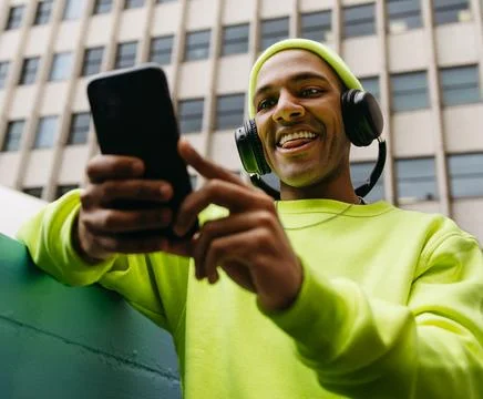 Low angle portrait of young multiracial man using smartphone with headphone.. Stock Photos