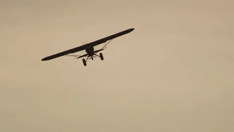 Low angle pull up focus of Super Cub plane flying across hazy sky at evening Stock Footage 252382745