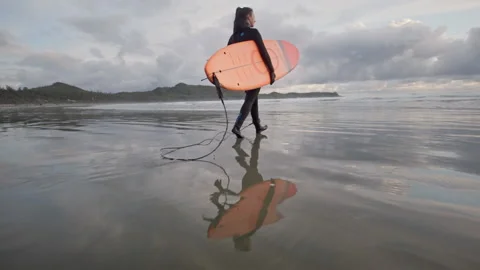 Low angle reflection of surf girl walking to the ocean with surfboard at sunset 库存影片 206470556