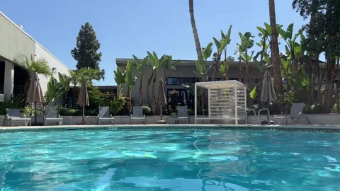 Low angle resort pool view toward empty lounge chairs, cabana and tropical Stock Footage 345369805