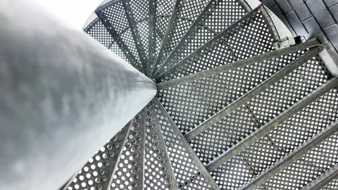 Low-angle rotating shot looking up at the center of a perforated metal spiral st Vídeos de archivo 332860335