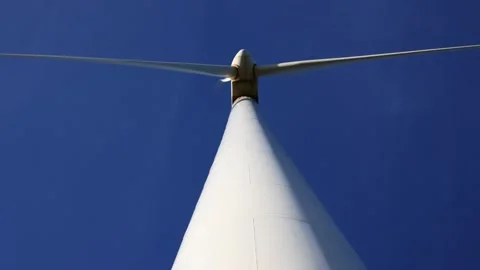 Low angle of rotating wind turbine blades set against a vibrant blue sky Stock Footage 294976135
