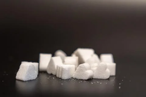 Low angle row of mixed sugar cubes and heart shaped sugar pieces on a dark Stock Photos