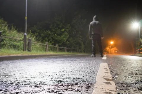 A low angle, shallow depth of field with a hooded figure standing on a road Stock Photos