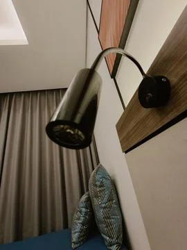 Low-angle shot of a black adjustable wall lamp next to a bed with patterned.. Stock Photos