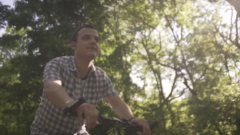 Low angle shot of calm happy middle age man in plaid shirt riding slow urban bik Stock Footage 132672496