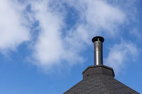 A low angle shot captures a black metallic chimney on top of a dark shingle r Foto stock