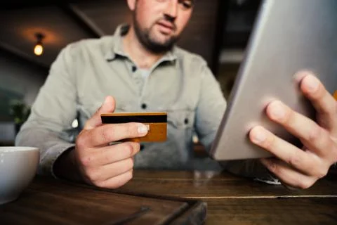Low angle shot of concerned, handsome male with credit card and tablet in hand Stock Photos