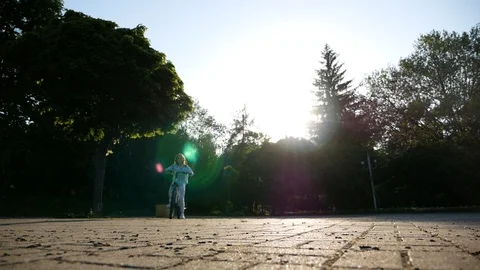 Low angle shot of a cute little girl riding a bike in the city park, alley in a Stock Footage 99361846