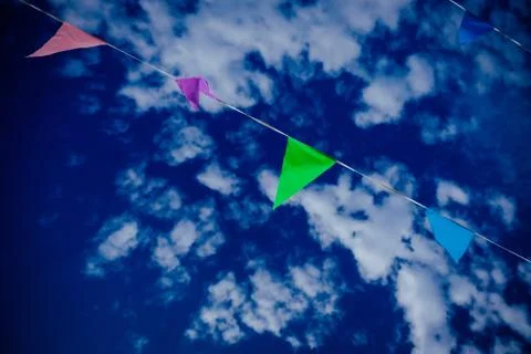 A low angle shot of different color flags on a rope with a blue cloudy sky in Stock Photos