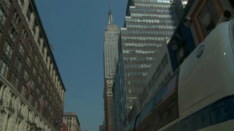 Low angle shot of Empire State Building with bus pulling away from curb, day. 스톡 동영상 108788496