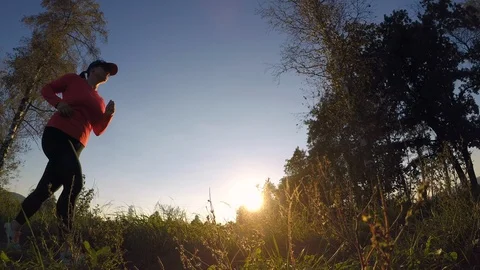 Low angle shot of a female runner passing by in nature at sunset Stock Footage 95501351
