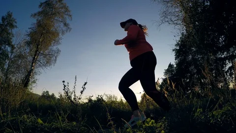 Low angle shot of a female runner passing by on a gravel road at sunset Stock Footage 95501425