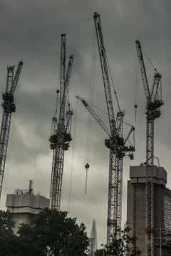 Low angle shot of four construction cranes against a cloudy gloomy sky Stock Photos