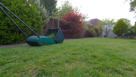 Low angle shot of a gardener mowing the lawn in a UK garden 動画素材 129246963