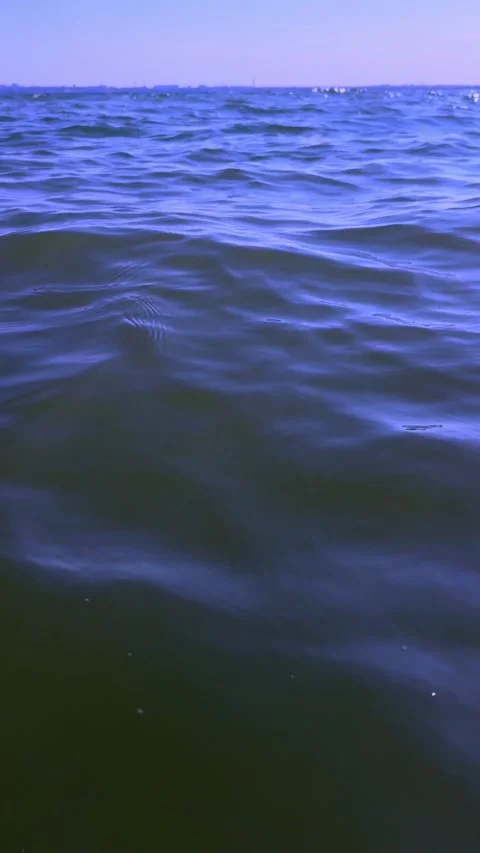 Low angle shot gliding over deep blue ocean waves with a purple-tinted sunset Stock Footage 341464503