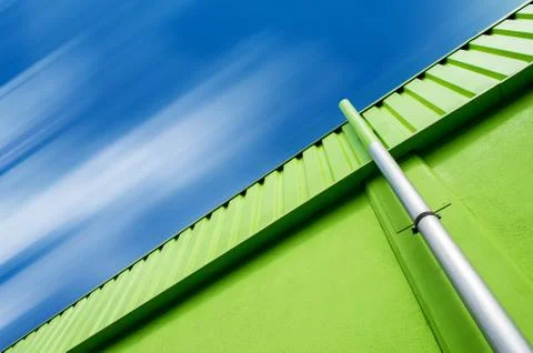 Low angle shot of a green building with a gray pipe under the cloudy sky Stock Photos