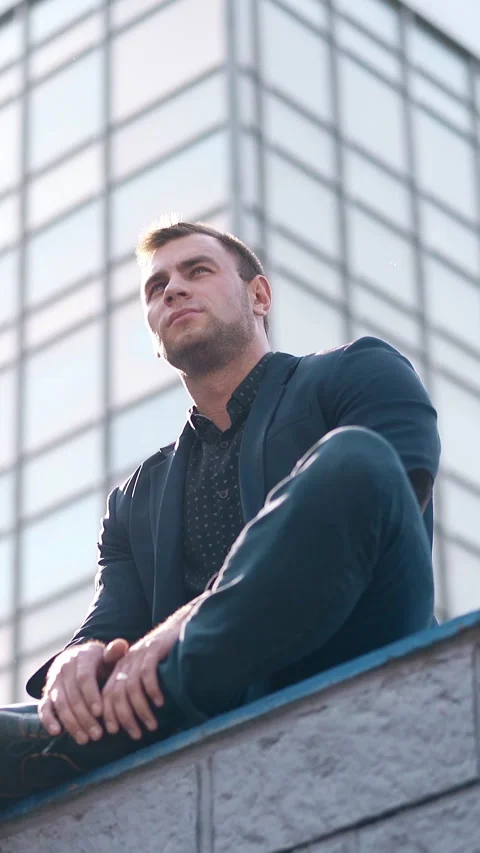 Low angle shot handsome man sits on parapet against building Stock Footage 308001852