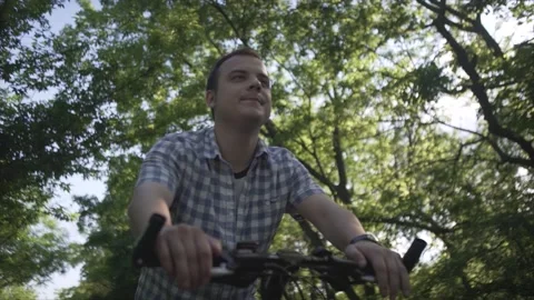 Low angle shot of happy calm middle age man in plaid shirt riding slow urban bic Stock Footage 132672452