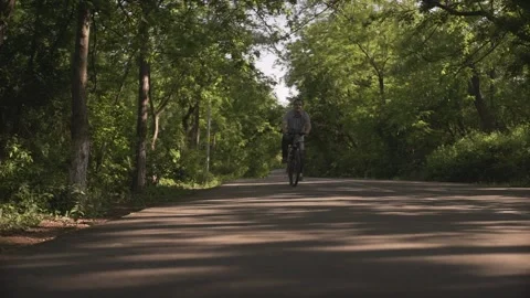 Low angle shot of happy middle aged man riding bike on empty bicycle road throug 動画素材 132672562