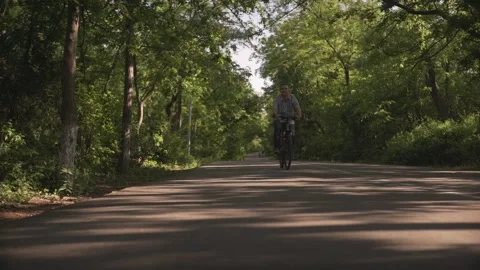 Low angle shot of happy middle aged man riding bicycle on empty bike road throug Stockbeeldmateriaal 132672575