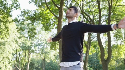 Low Angle Shot of Indian man spinning with their arms outstretched amongst trees Stock Footage 125094994