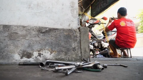 Low angle shot of Indonesian man repairing motorcycles in a local garage, Bali Stock Footage 140294136