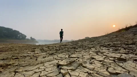 Low angle shot of jogger running on drought river bed, cracked soil, misty Stock Footage 231458244
