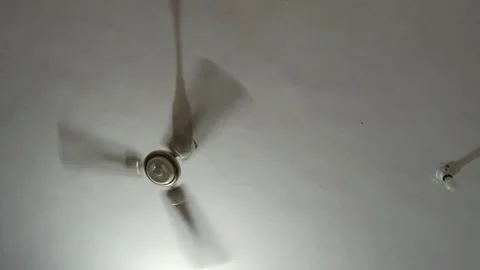 A low-angle shot in a living room shows a white, three-bladed ceiling fan motion Stock-Footage 343784317