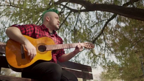 Low angle shot of a man with a green mohawk playing guitar outside Stock-Footage 139314088