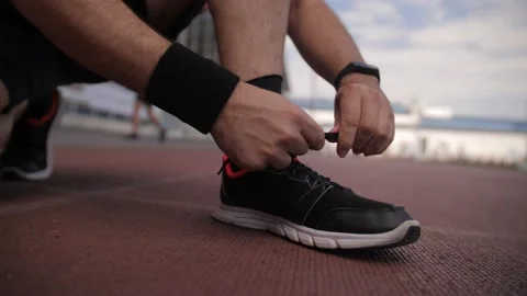 A low-angle shot of a man tying his shoelaces on black sneakers in a stadium. 動画素材 203572378