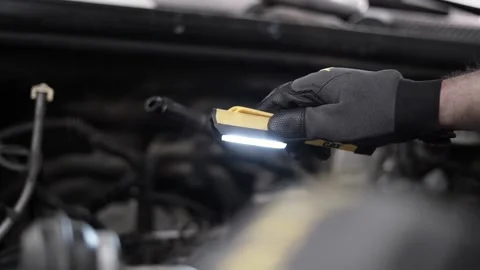 Low-angle shot of a mechanic using a light to check in a car engine bay Stock Footage 235687129