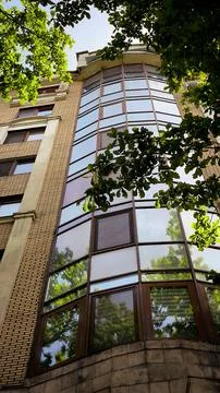 Low angle shot of modern building facade with glass windows and green trees. Fotos Stock