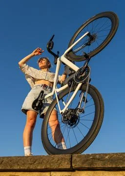 Low angle shot of modern young woman standing on stone parapet, holding sport Stock Photos