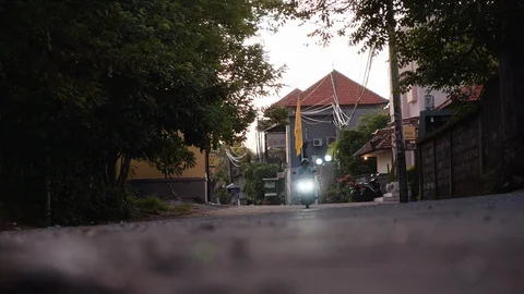 Low angle shot of a motorcycle approaching the camera on a small town road, Bali Stock Footage 140267196