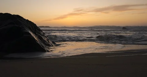 Low angle shot over beach at dusk with big rock on left Vídeos de archivo 116586339