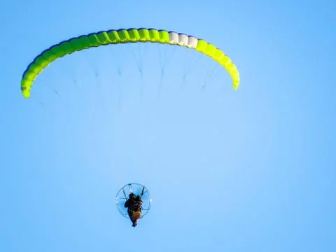Low angle shot of a person in powered paragliding under a clear blue sky Stock Photos