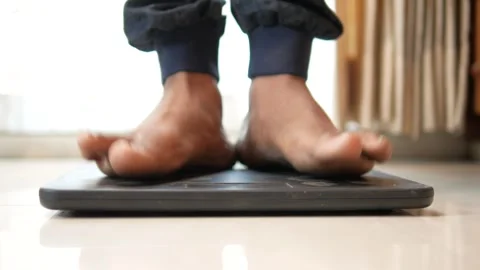 A low-angle shot of a person's bare feet stepping on a digital weight scale.. Stock-Footage 332578705