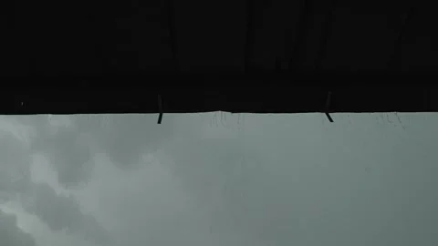 A low-angle shot of rain pouring from a dark roof gutter Stock Footage 340819595